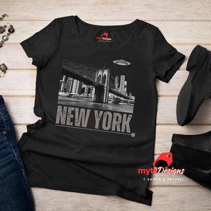 Black soft casual tee showing the New York City skyline with a stylized spaceship graphic soaring above, flat lay on wooden boards
