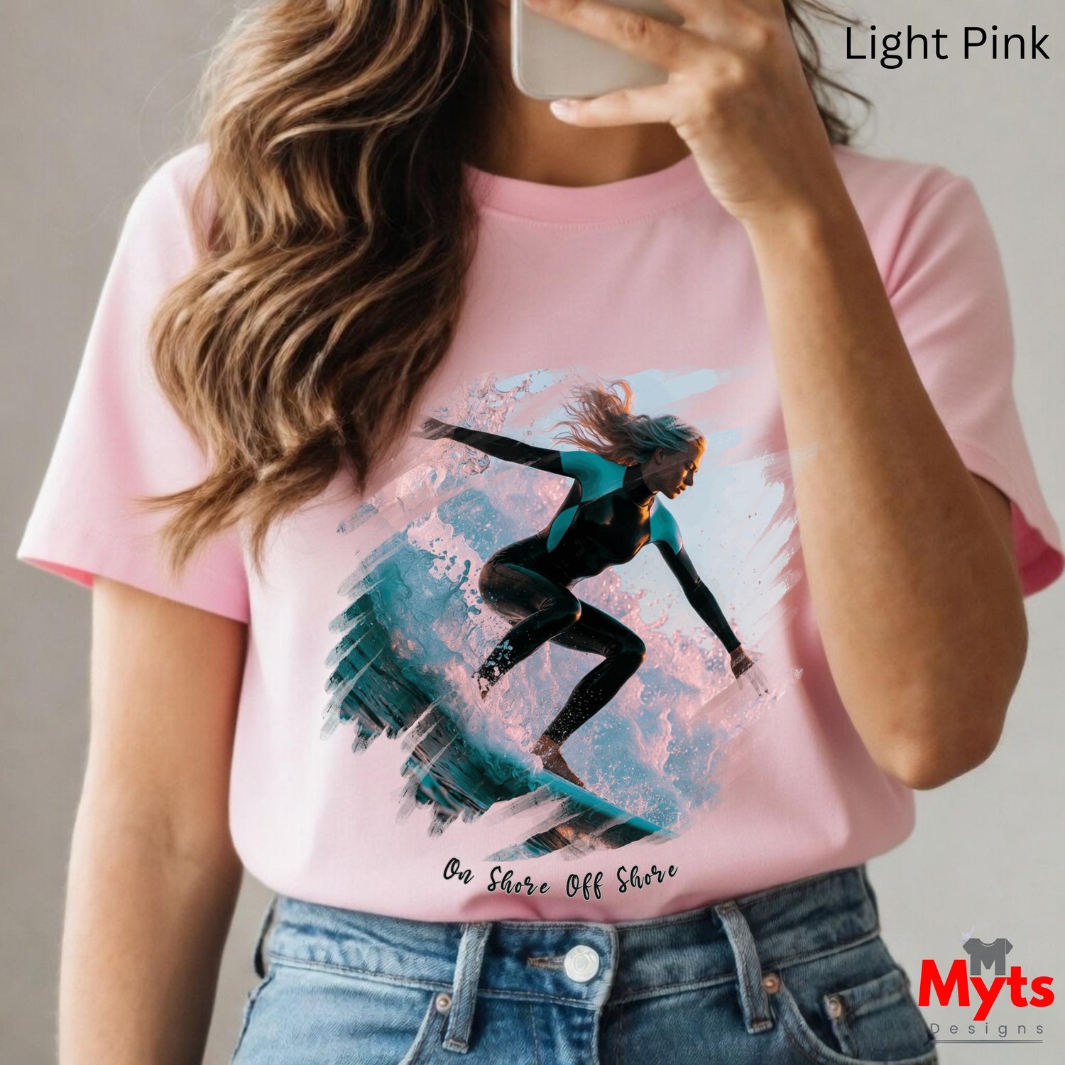 Person wearing a pink t-shirt with a graphic design of a person surfing, holding a phone.