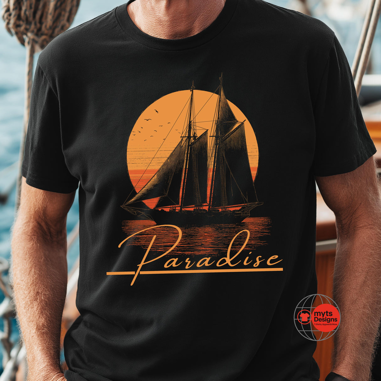 Black t-shirt with a sailboat design and 'Paradise' text on a person standing on a boat.