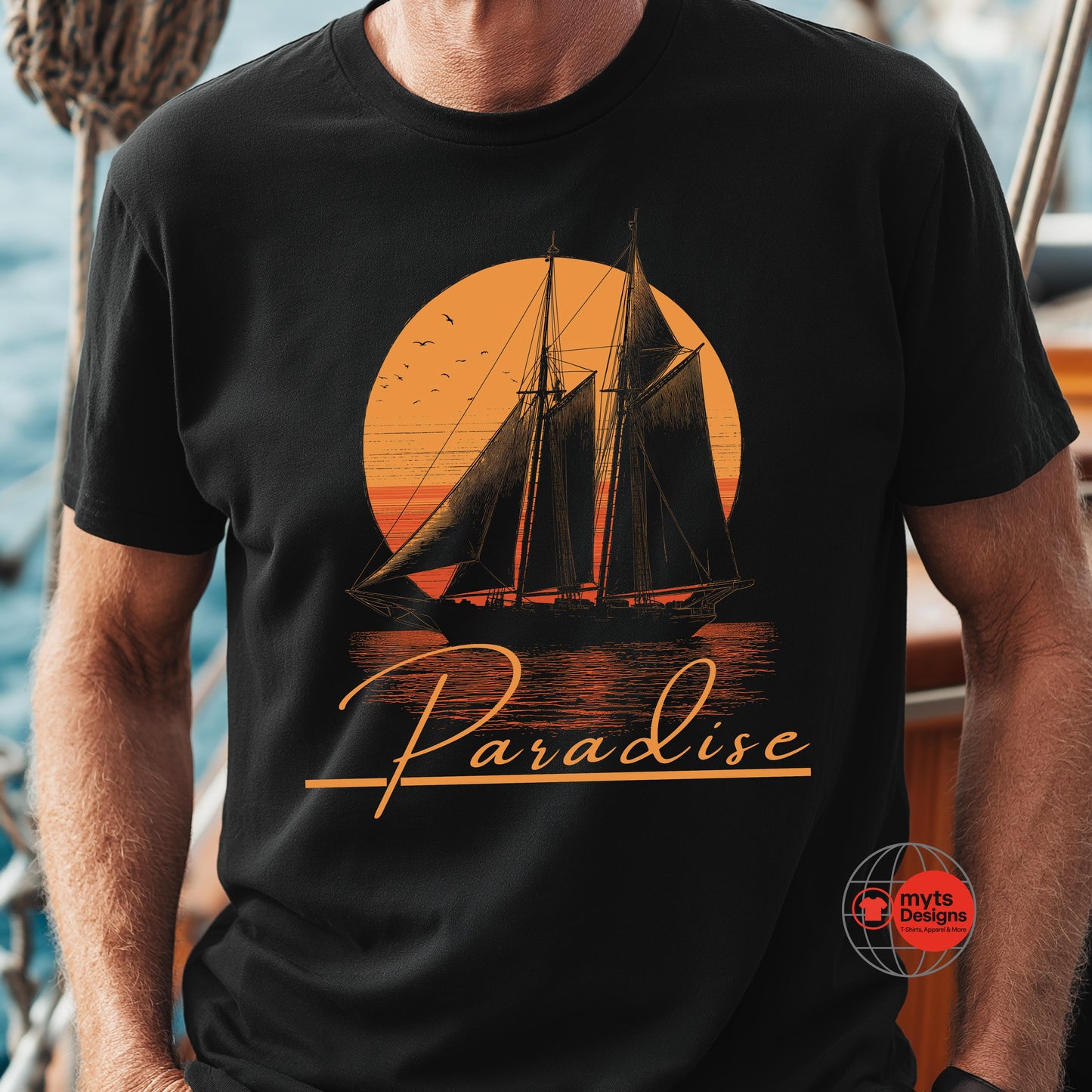 Black t-shirt with a sailboat design and 'Paradise' text on a person standing on a boat.