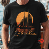 Black t-shirt with a sailboat design and 'Paradise' text on a person standing on a boat.