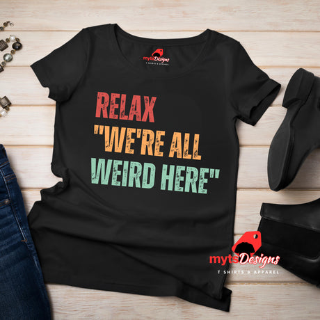 A flat lay view of a black Retro-style casual tee featuring bold distressed vintage typography reading “Relax — We’re All Weird Here,” printed on ultra-soft Gildan 64000 cotton.