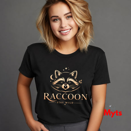 A smiling blonde woman wearing a black short-sleeve T-shirt with a gold raccoon graphic and the words 'RACCOON' and 'STAY WILD' on the front, photographed against a plain gray studio background.