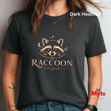 A woman wearing a dark heather charcoal t-shirt with a gold graphic of a raccoon face, stars, and the text 'RACCOON STAY WILD'. The image has a 'Dark Heather' color label overlay and a 'Myts designs' watermark in the bottom right corner.