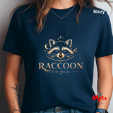 A navy blue short-sleeve t-shirt worn by a model, featuring a gold graphic of a raccoon face with stars and the text 'RACCOON STAY WILD'. The word 'Navy' is printed in white in the top right corner, and a red 'Myts Designs' logo is visible in the bottom right corner.