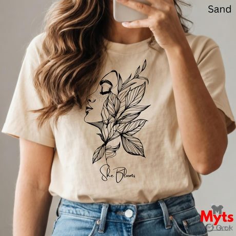 Person wearing a Sand t-shirt with a floral design and text, holding a phone.