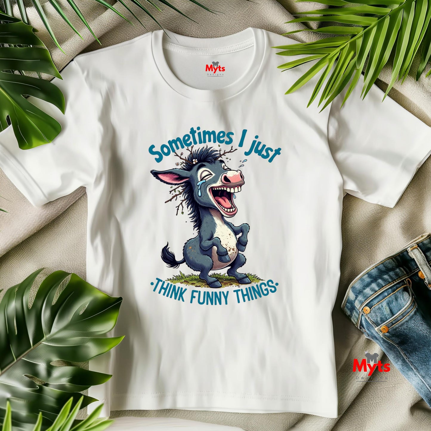 White t-shirt with cartoon donkey graphic and text 'Sometimes I just think funny things' on a beige surface with green leaves.