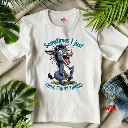 White t-shirt with cartoon donkey graphic and text 'Sometimes I just think funny things' on a beige surface with green leaves.