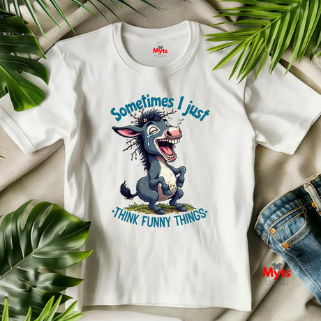 White t-shirt with cartoon donkey graphic and text 'Sometimes I just think funny things' on a beige surface with green leaves.