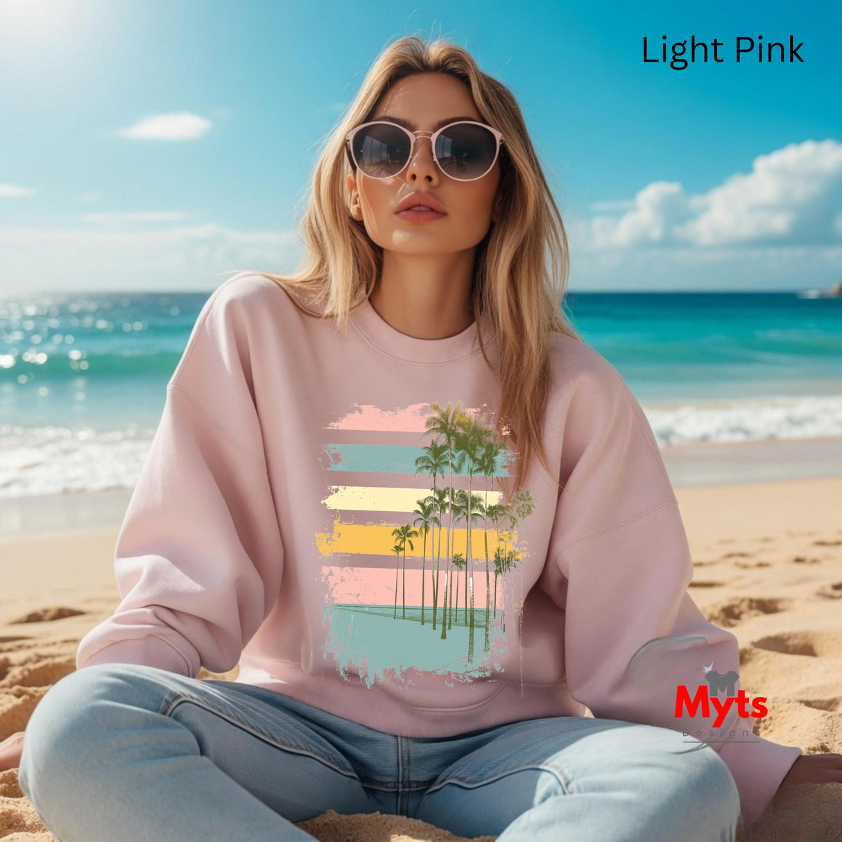 Woman wearing a light pink sweatshirt with a beach design on a beach setting, featuring the brand 'Myts'.