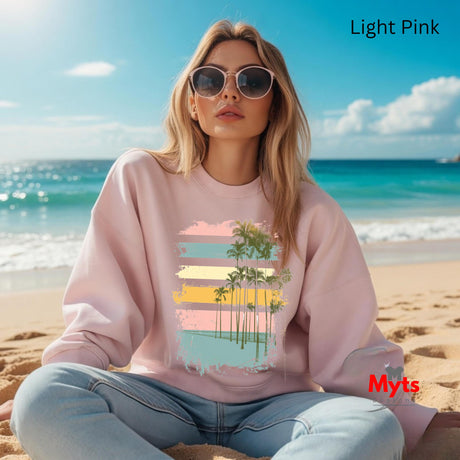 Woman wearing a light pink sweatshirt with a beach design on a beach setting, featuring the brand 'Myts'.