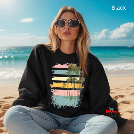 Woman wearing a black sweatshirt with a colorful design sitting on a beach.