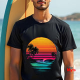 Person wearing a black t-shirt with a colorful sunset and palm tree design, standing by a surfboard on a beach.