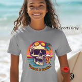 Person wearing a gray t-shirt with a skull graphic and sunglasses on a beach.