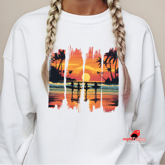 Close-up of a white sweatshirt worn by a woman with blonde braids, showcasing a vibrant graphic of a tropical beach at sunset with silhouetted surfers, palm trees, and ocean waves.