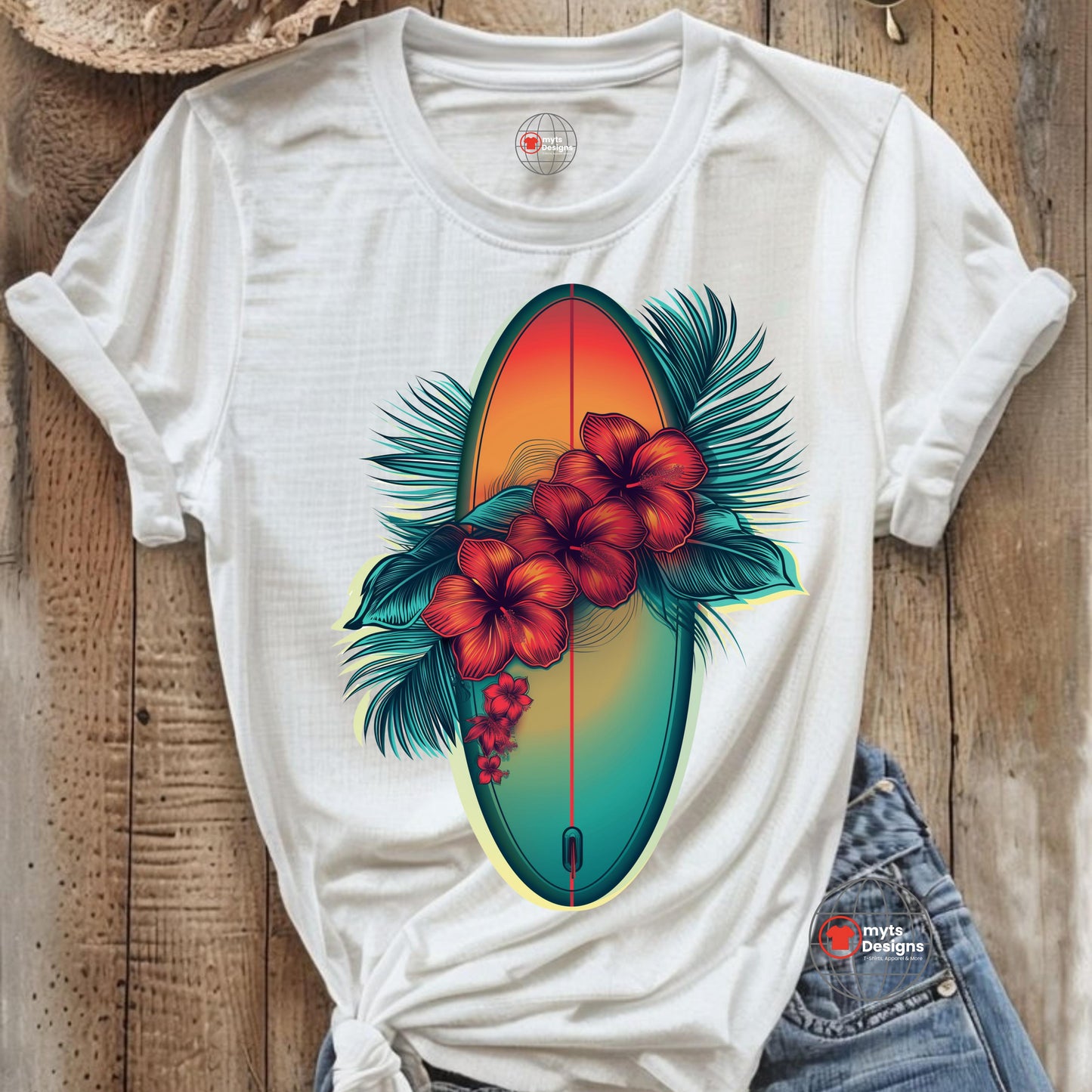 A white T-shirt laid on a wooden surface featuring a vibrant graphic of a surfboard in sunset hues surrounded by red hibiscus flowers and green palm leaves, styled with rolled sleeves and denim shorts.