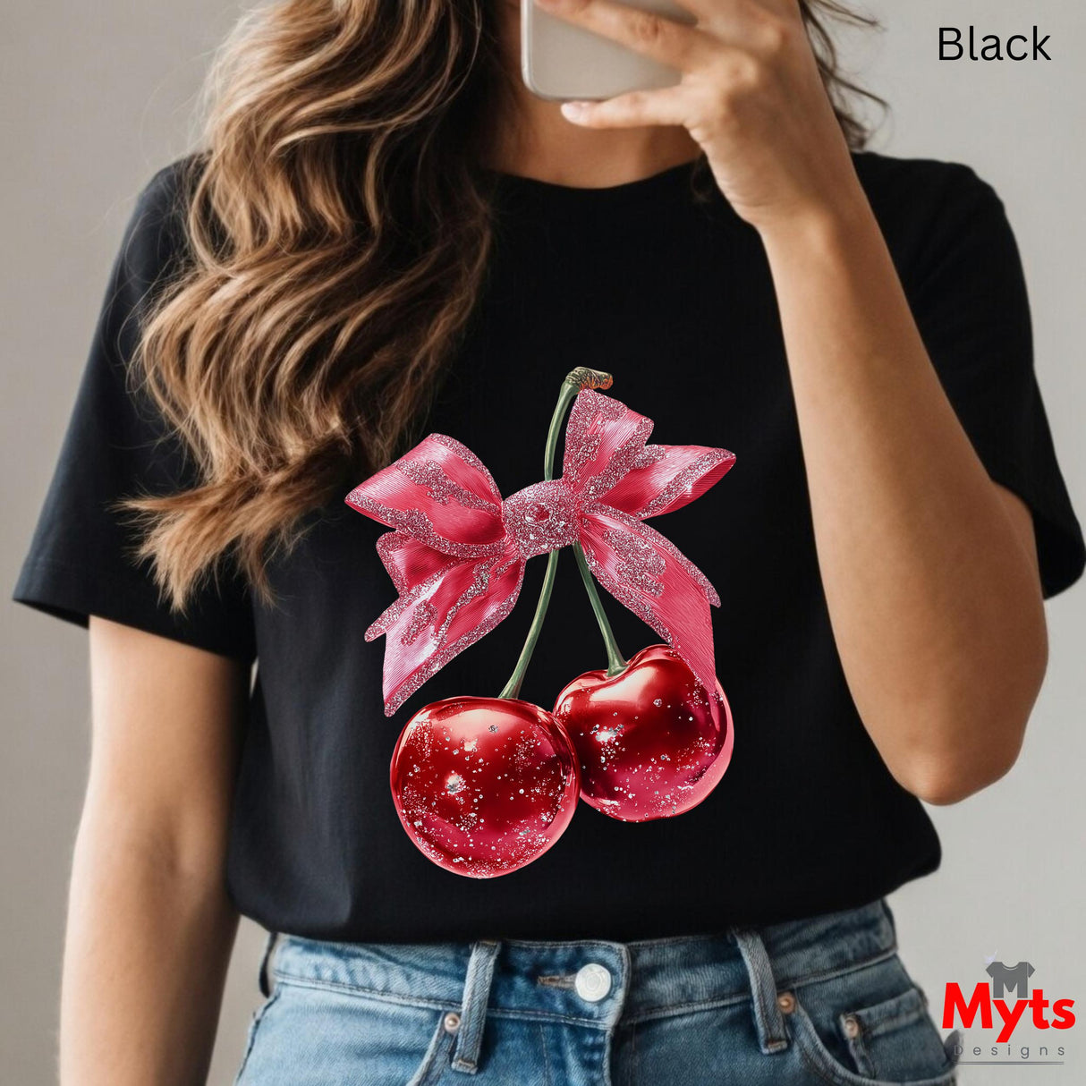 Person wearing a black t-shirt with red cherries and a pink bow design, holding a phone.