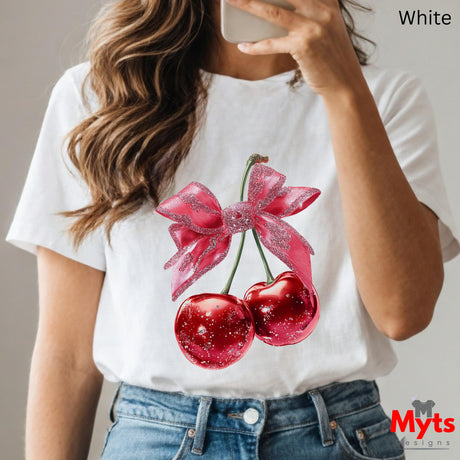 Person wearing a white t-shirt with red cherries and pink bow design, holding a phone.