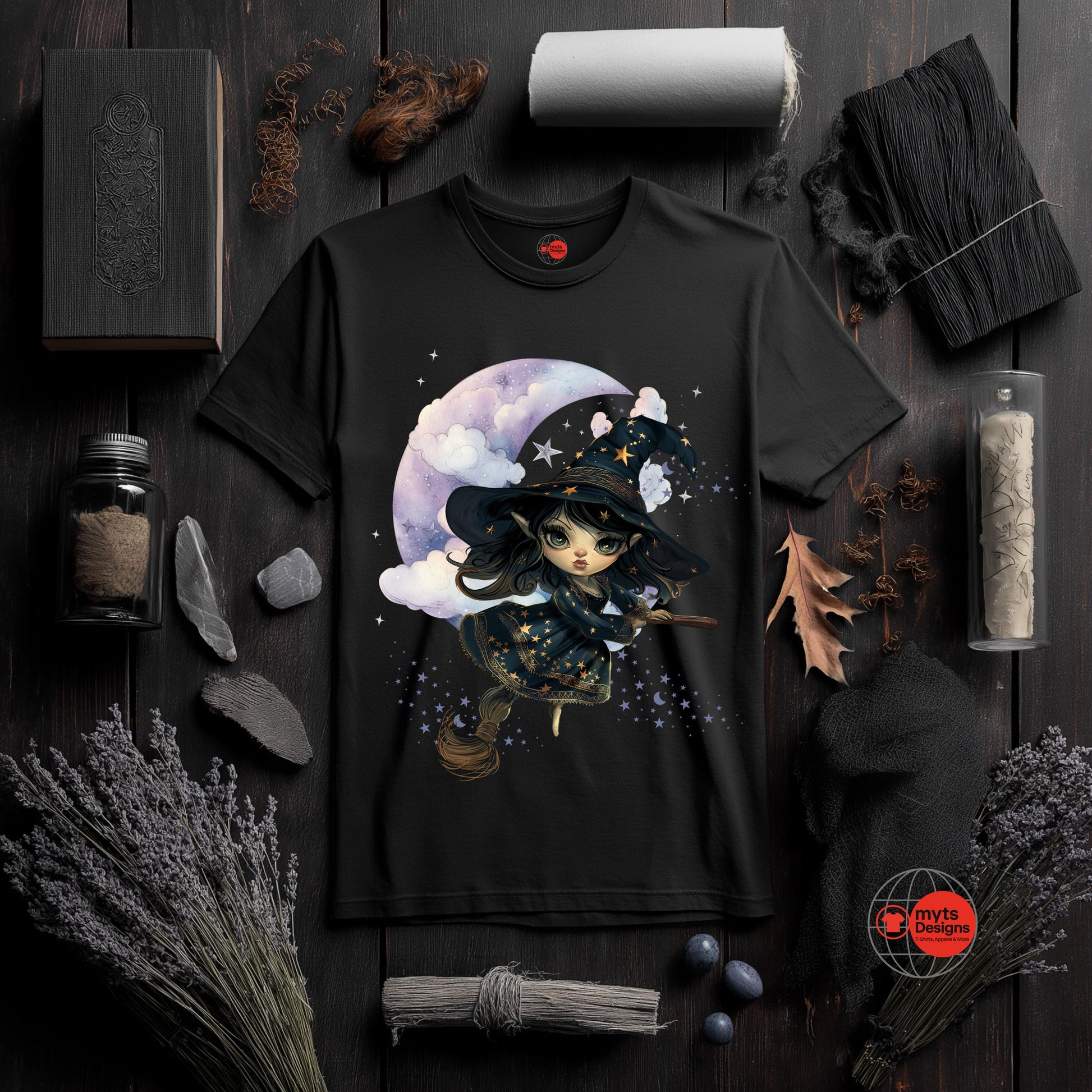 Black t-shirt with a witch design on a dark wooden surface with decorative items.