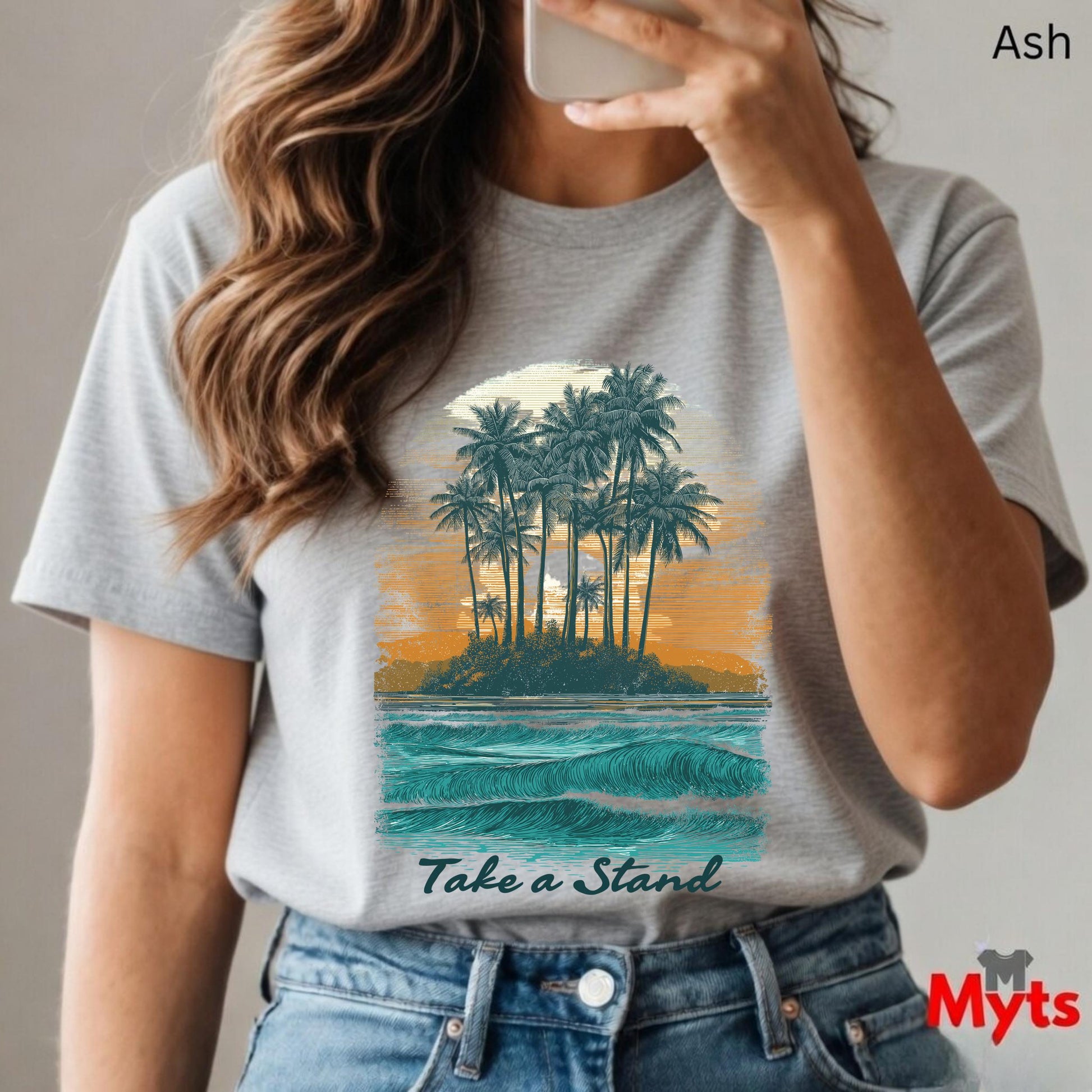 Person wearing a gray t-shirt with a tropical island graphic and 'Take a Stand' text, holding a phone.