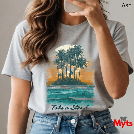 Person wearing a gray t-shirt with a tropical island graphic and 'Take a Stand' text, holding a phone.