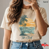Person wearing a sand t-shirt with a palm tree and sunset design, text 'Take a Stand', and jeans.