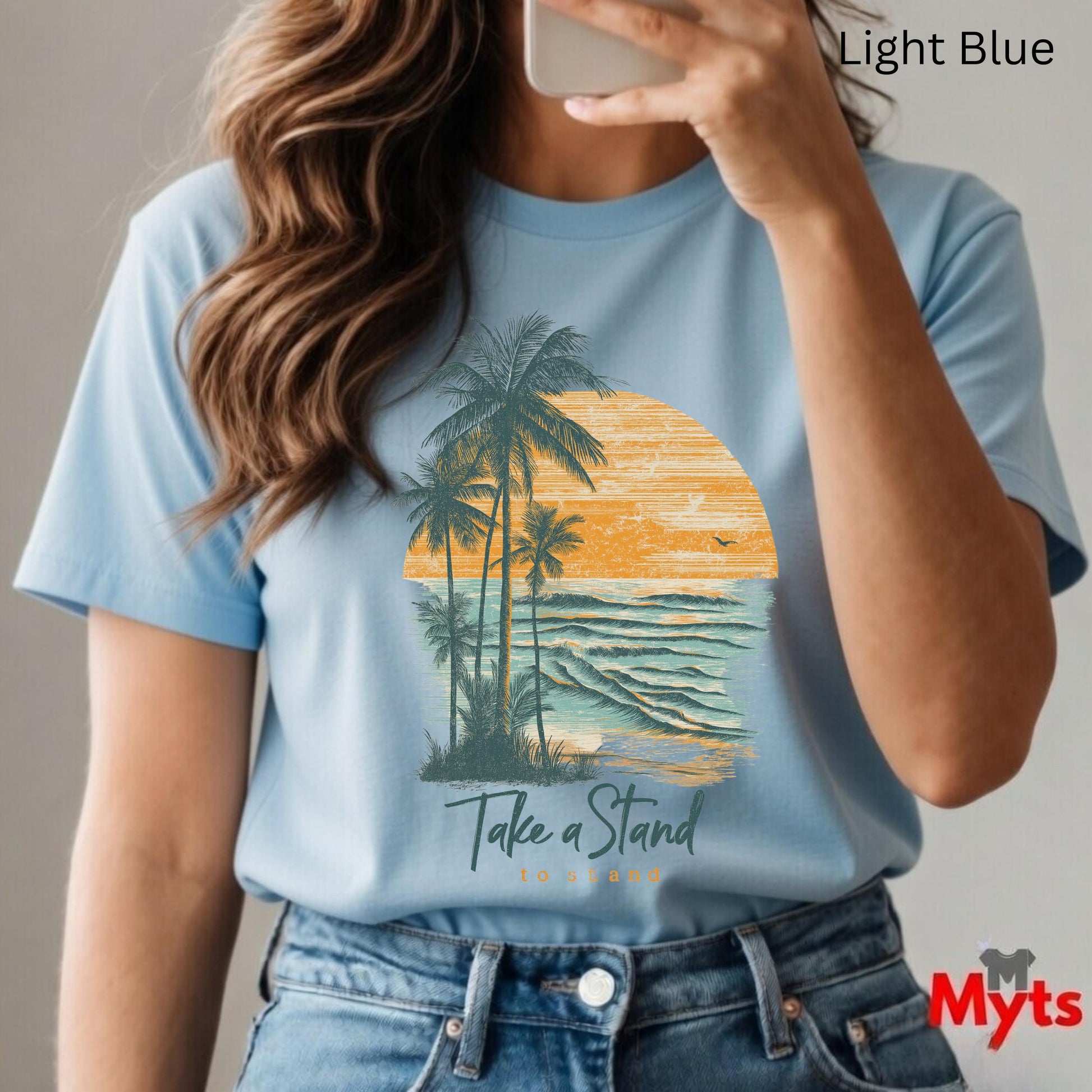Person wearing a light blue t-shirt with a palm tree and sunset design, taking a selfie.