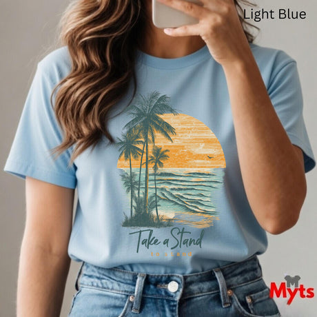 Person wearing a light blue t-shirt with a palm tree and sunset design, taking a selfie.