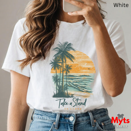 Person wearing a white t-shirt with a palm tree and sunset design, text 'Take a Stand', and jeans.