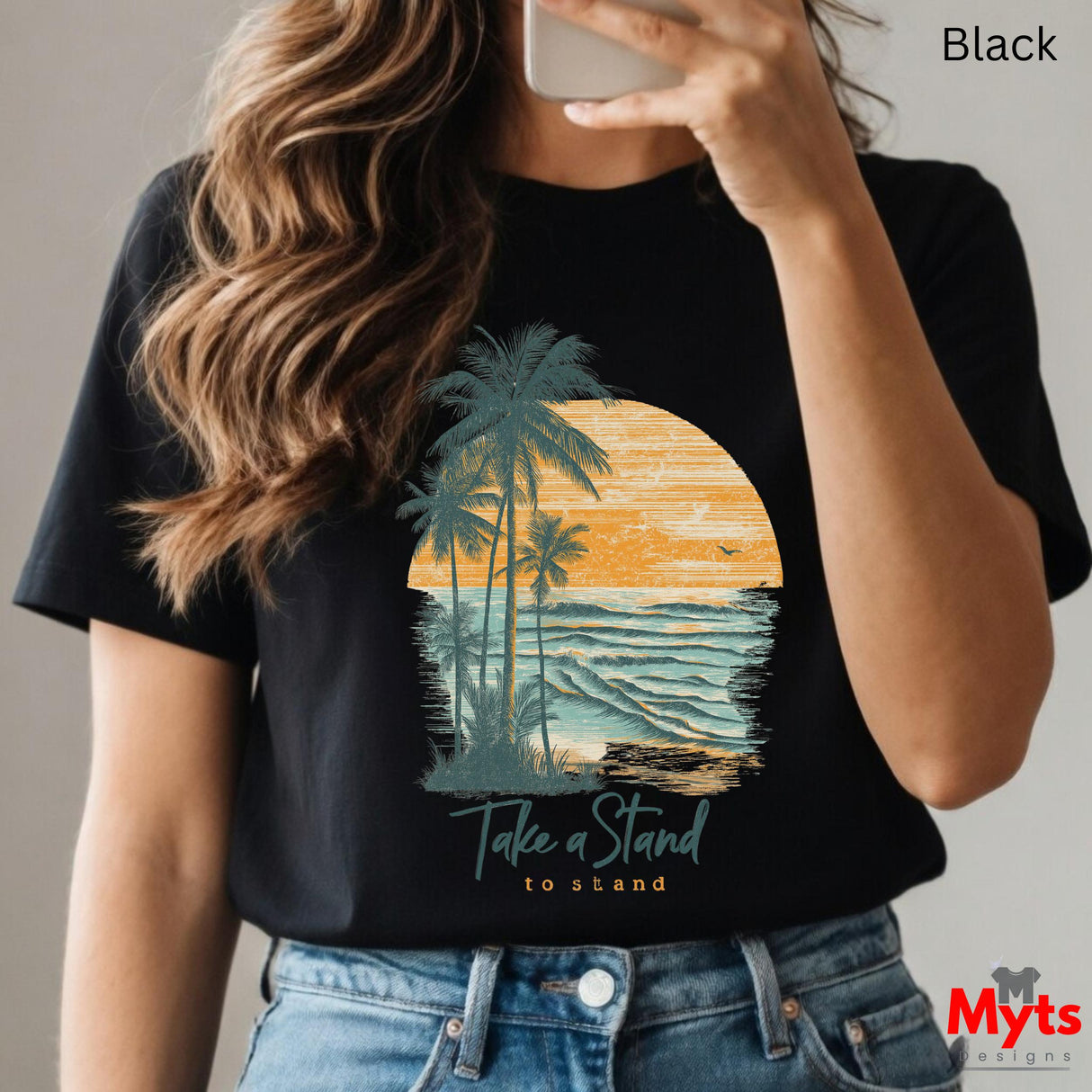 Person wearing a black t-shirt with a palm tree and sunset design, holding a phone.