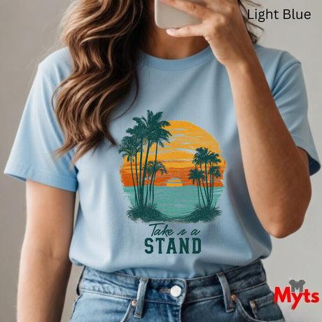 Person wearing a light blue t-shirt with a palm tree design and 'Take a Stand' text, taking a selfie.