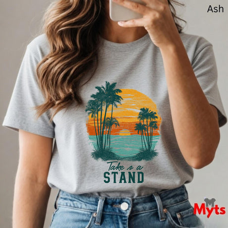 Person wearing a t-shirt with a palm tree and sunset design, text 'Take a Stand', and jeans.