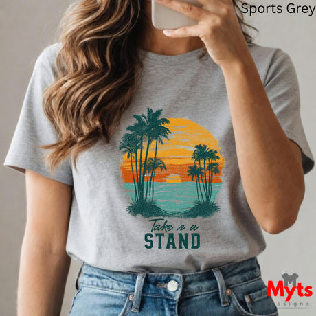 Person wearing a gray t-shirt with a tropical design and 'Take a Stand' text, holding a phone.