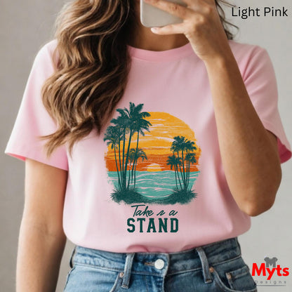 Person wearing a pink t-shirt with a palm tree design and 'Take a Stand' text, holding a phone.