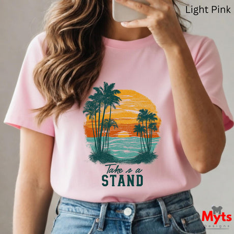 Person wearing a pink t-shirt with a palm tree design and 'Take a Stand' text, holding a phone.
