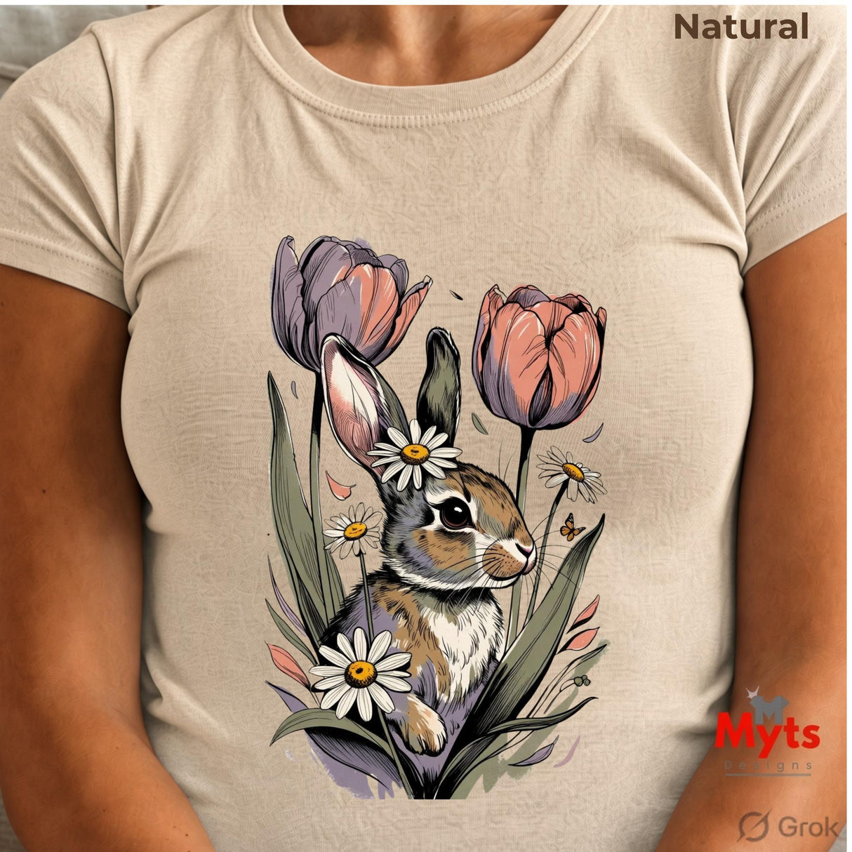 A person wearing a lNatural short-sleeve T-shirt with a large printed illustration of a rabbit surrounded by tulips and daisies. The top right corner reads 'Natural', and the bottom right shows the 'Myts Designs' and 'Grok' logos.