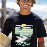 Person wearing a black t-shirt with a beach graphic and 'The Swell' text, holding a surfboard on a beach.