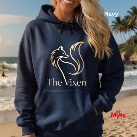 Person wearing a navy hoodie with 'The Vixen' logo on a beach