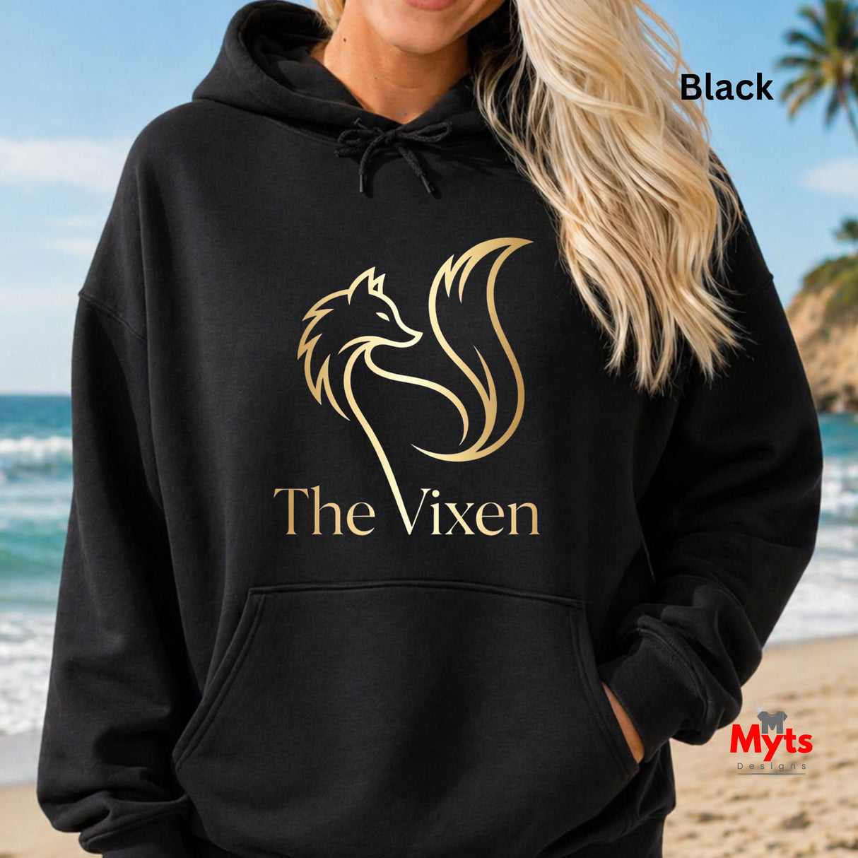 Person wearing a black hoodie with 'The Vixen' logo on a beach