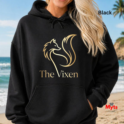 Person wearing a black hoodie with 'The Vixen' logo on a beach