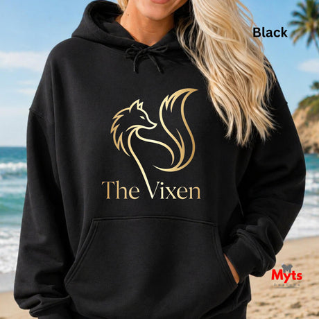 Person wearing a black hoodie with 'The Vixen' logo on a beach