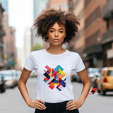 A white t-shirt features a striking, modern geometric design with overlapping vibrant shapes in shades of red, blue, yellow, pink, and black. The bold abstract pattern creates an energetic and contemporary look in the center of the shirt. The t-shirt is worn by a woman standing confidently on a city street, with her hands on her hips. A small red bird logo with the text “mytsDesigns” appears in the bottom right corner.

