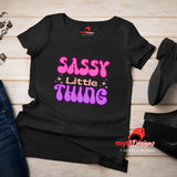 Flat Lay view of “Sassy Little Thing” T-shirt with groovy 70s-style typography on black cotton tee
