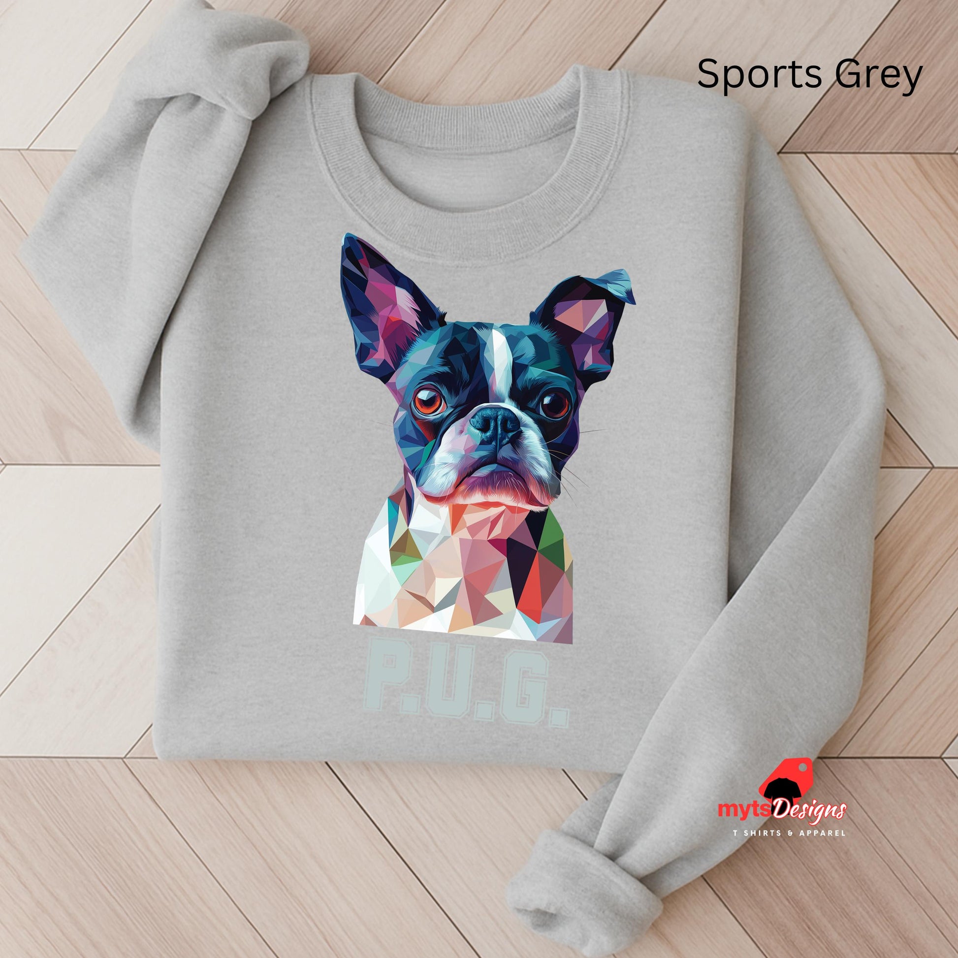 A sports grey sweatshirt displayed on a wooden surface featuring a vibrant polygon-style dog portrait with the text “P.U.G.” below, designed by MytsDesigns