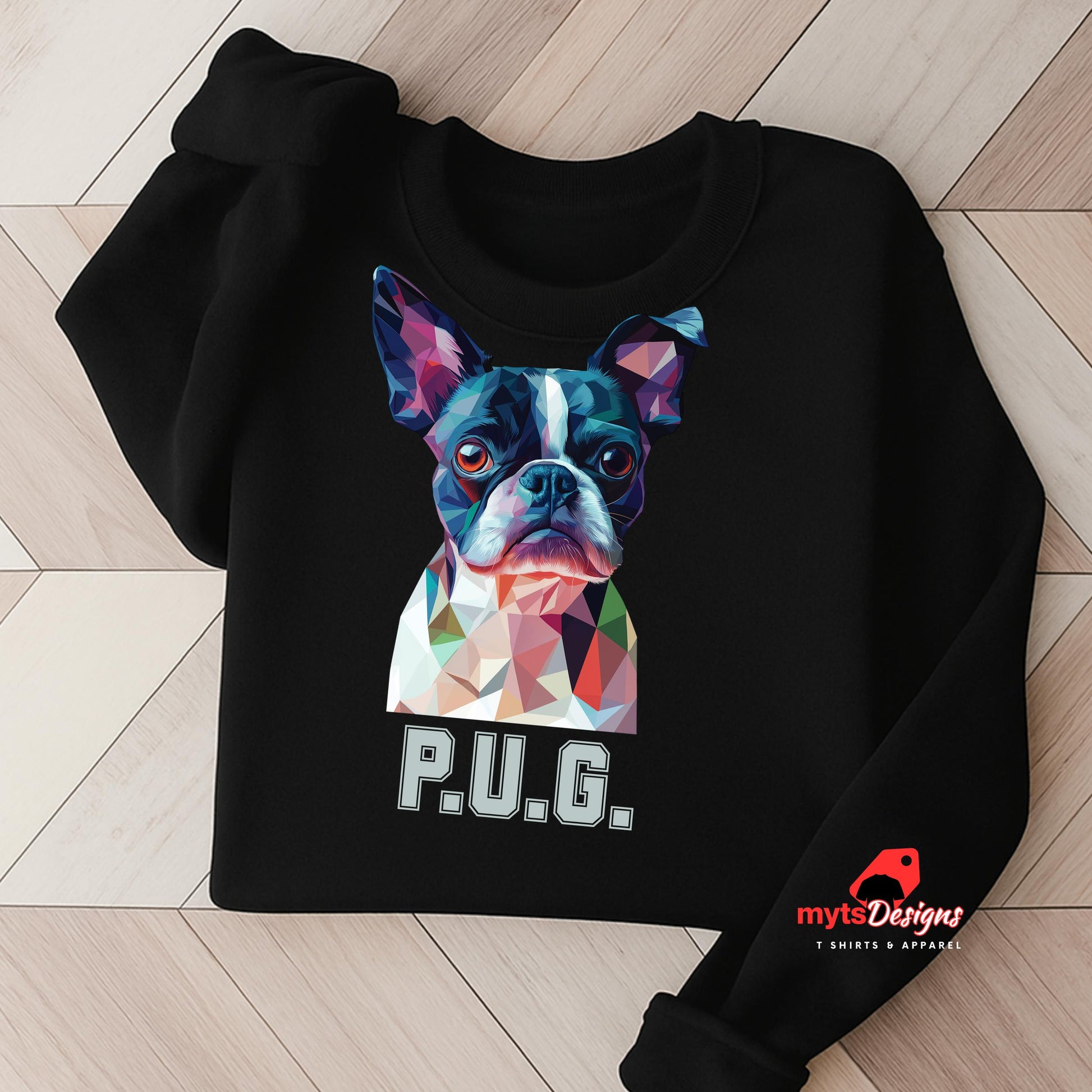 A black sweatshirt displayed on a wooden surface featuring a vibrant polygon-style dog portrait with the text “P.U.G.” below, designed by MytsDesigns