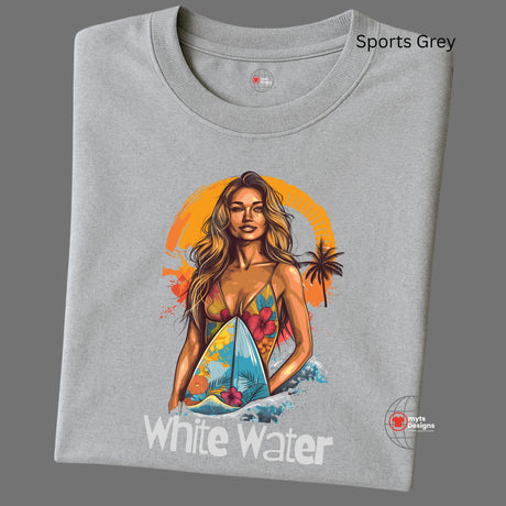 A folded grey T-shirt featuring a vibrant illustration of a confident woman in a floral bikini holding a surfboard with ocean waves and an orange tropical sunset in the background. Below the graphic is the text “White Water.” 