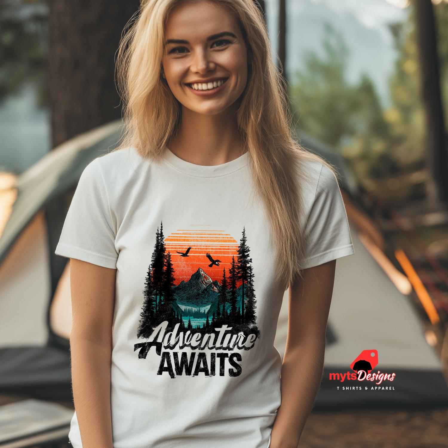 Woman wearing a 'Adventure Awaits' t-shirt with a scenic design, standing in front of a tent.