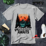 Gray t-shirt with 'Adventure Awaits' design on a textured surface with accessories.
