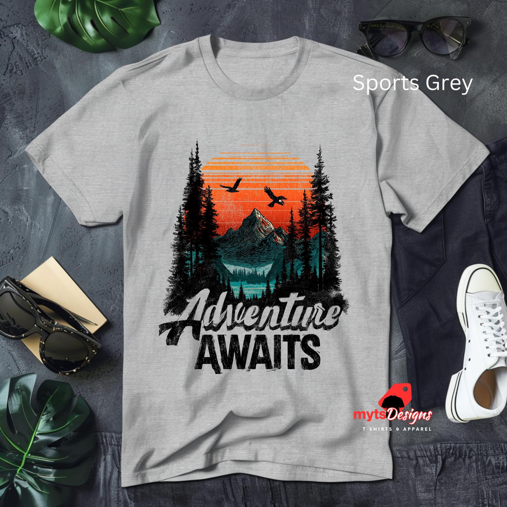 Gray t-shirt with 'Adventure Awaits' design on a textured surface with accessories.