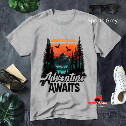 Gray t-shirt with 'Adventure Awaits' design on a textured surface with accessories.